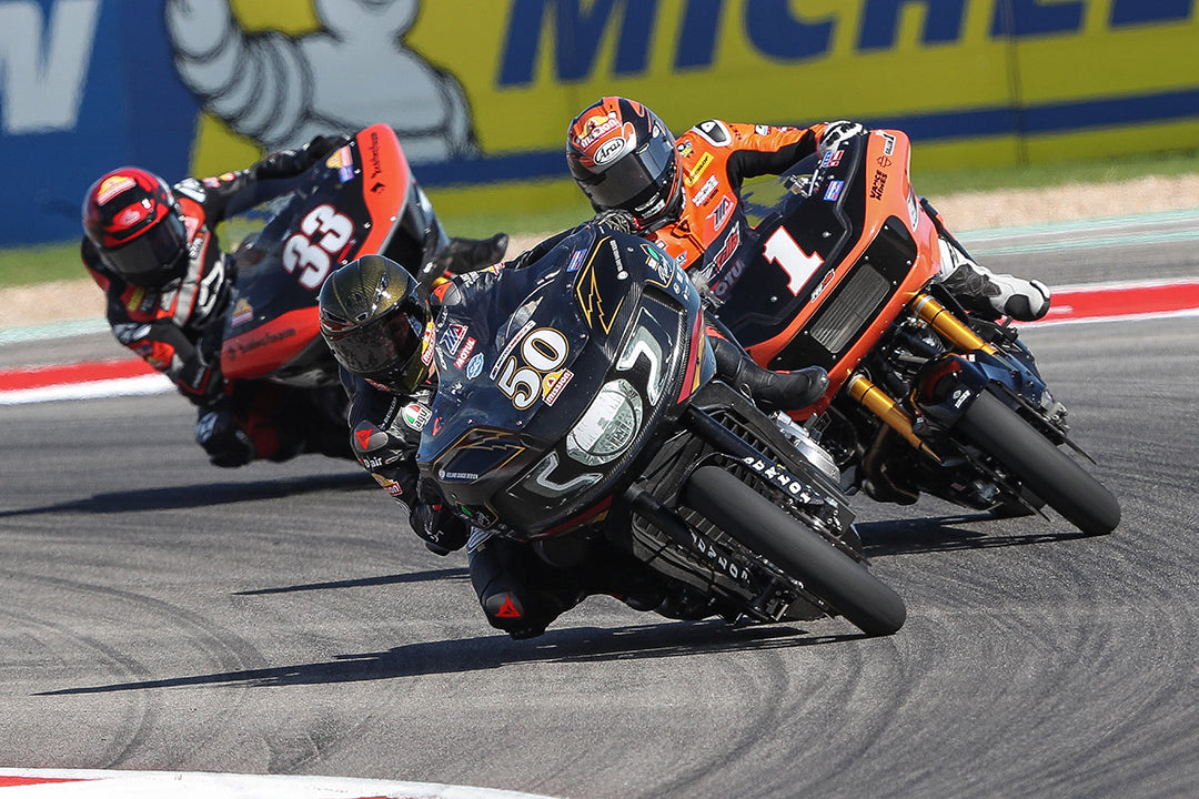 Intense cornering action captured at the Circuit of the Americas with three motorcycles closely contesting a corner, showcasing the skill and precision required at high speeds, under the vibrant Michelin and Red Bull banners.