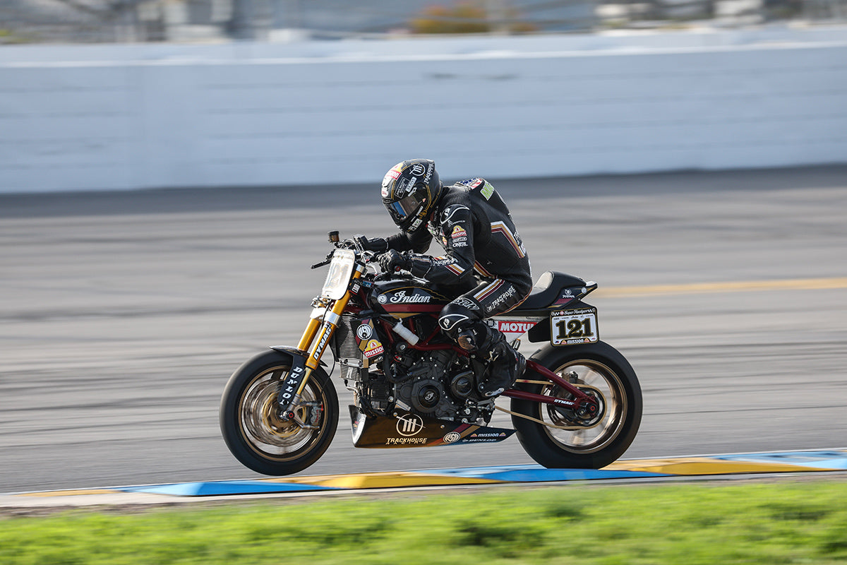 Action shot of a racing motorcycle with Dymag wheels in motion on a racetrack, showing the rider in full gear leaning into a turn.