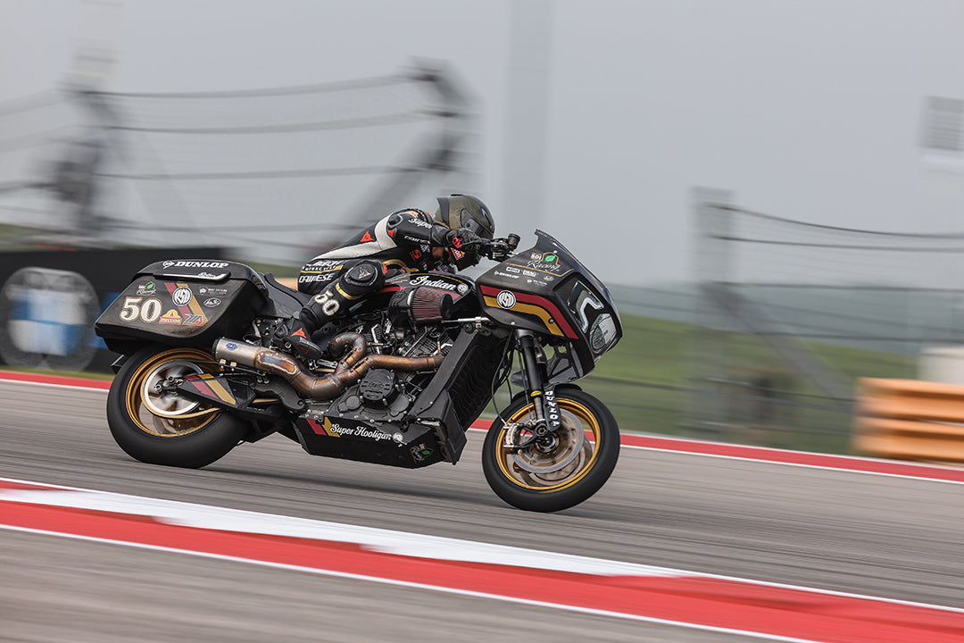 A solo motorcycle racer, number 50, speeds along a red and white curb at the Circuit of the Americas, with a blurred background that conveys the high speed and focus required in professional motorcycle racing.