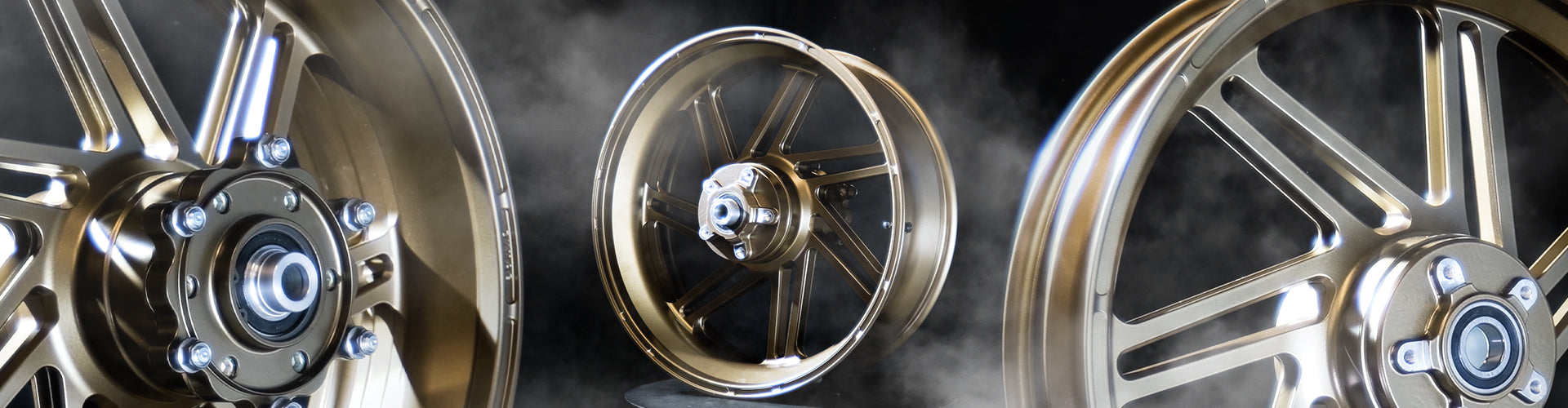 A detailed view of three golden Dymag racing wheels arranged sequentially against a smoky background. The focus gradually shifts from a close-up of the wheel hub in the foreground to a full view of the wheel in the background, highlighting the sleek design and metallic finish of the wheels.