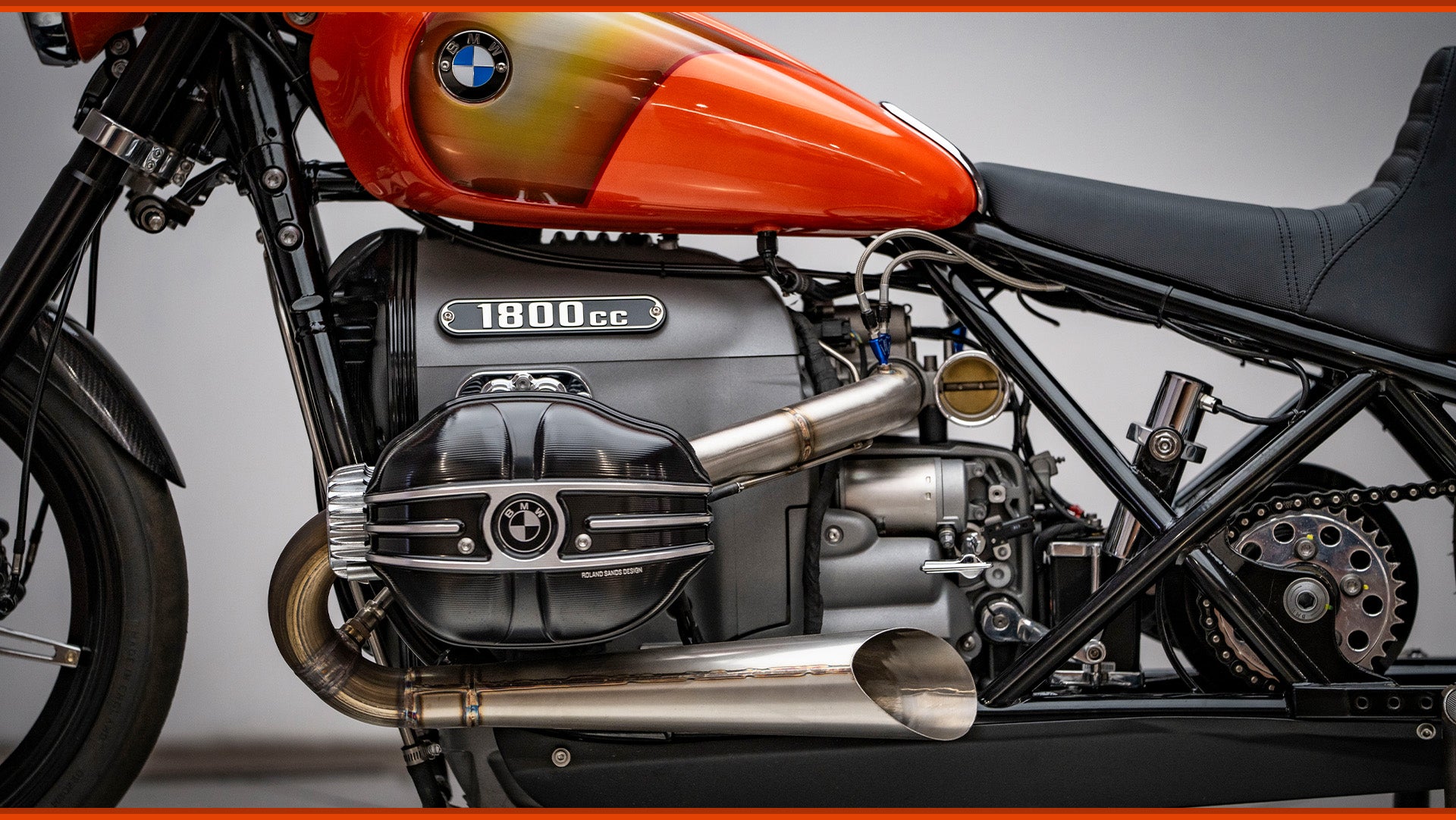 close up of left side profile photo of the orange RSD x BMW R18 Dragster II motorcycle. focus is on valve cover and exhaust