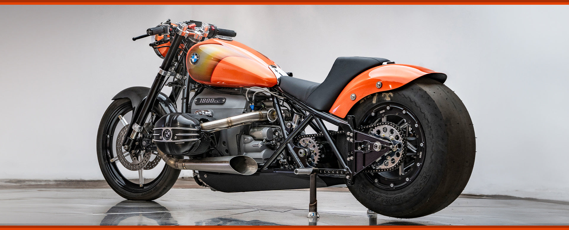 Back left side photo of the orange RSD x BMW R18 Dragster II motorcycle. You can really see how big the rear tire is 